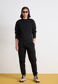 Set di felpa nera e pantaloni, realizzato in tessuto morbido. Include un piccolo logo sul petto. Le calzature presentano una suola spessa con lacci.