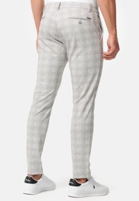 Pantaloni gri deschis, slim-fit, cu un model discret în carouri, două buzunare posteriori cu nasturi, asortați cu adidași albi cu un accent negru.