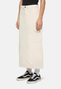 Beige bomulls-midi kjol med sidofickor, bältesloopar och rak silhuett, ihop med svarta sneakers och vita strumpor.