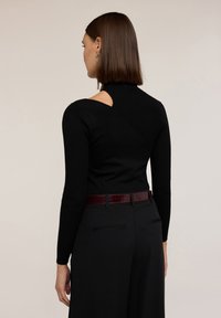 Černý žebrovaný svetr s dlouhými rukávy a jedinečným výřezem na zádech, kombinovaný s kalhotami s vysokým pasem a lesklým vínovým pásem.