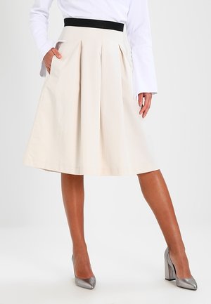 Gelaagde beige rok met een zwarte elastische tailleband, tot op de knie, voorzien van zijzakken en een gladde katoenstructuur.