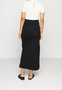 Svart maxikjol med en åtsittande midja och en mjuk textur, kombinerad med en vit ribbad topp med en nyckelhålsdetalj i ryggen.