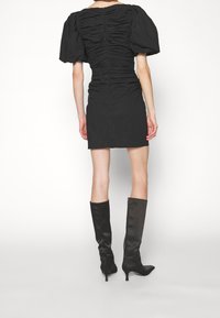 Svart figursydd klänning med rynkad textur, korta puffärmar och dragkedja i ryggen, tillsammans med knähöga svarta satinstövlar.