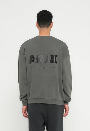 Gray oversized sweatshirt with a crew neckline, featuring a large black graphic text on the back, made from soft, textured fabric.