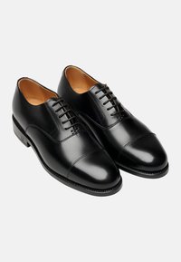 Schwarze Leder-Dressschuhe mit glatter Oberfläche, Kappenform, sechs Ösen zum Schnüren und kontrastierender beige Innensohle. Klassische Silhouette mit detaillierter Nahtverarbeitung.