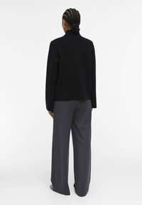Maglione nero a collo alto realizzato in materiale morbido, abbinato a pantaloni grigi a gamba larga. L'outfit presenta una silhouette rilassata e un design minimalista.