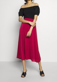 Zwart off-shoulder top met pofmouwen, gecombineerd met een vloeiende, knielange fuchsia rok. Zwarte open teen hakken maken de look compleet.