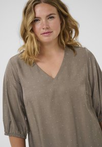 Blusa topo con escote en V, mangas cortas abullonadas y puntos blancos dispersos. Fabricada con un tejido suave de textura lisa y un corte relajado.