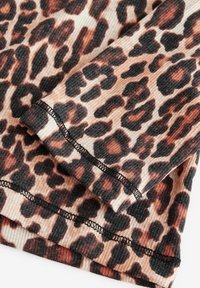 Gros plan d'un tissu côtelé avec un imprimé léopard marron et noir et une couture noire visible le long des bords pliés.