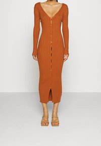 Robe midi côtelée couleur rouille avec manches longues, décolleté en V profond, fermeture par boutons et fente à l'avant. Portée avec des sandales à brides beige.