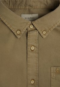 Camisa de botones beige de algodón, con un cuello clásico, una botonera de seis botones y un pequeño logo bordado en el bolsillo del pecho.