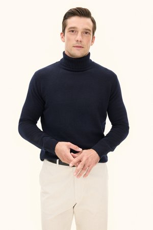 Marineblauer Rollkragenpullover aus weichem Stoff, mit geripptem Kragen und figurbetontem Schnitt, kombiniert mit hellen Hosen.