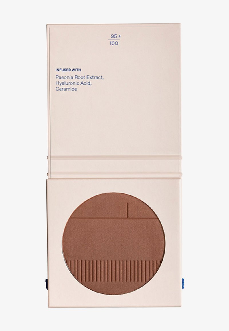 Contenant beige compact avec texte listant l'extrait de racine de pivoine, l'acide hyaluronique et la céramide, avec un compact cosmétique circulaire marron en dessous.