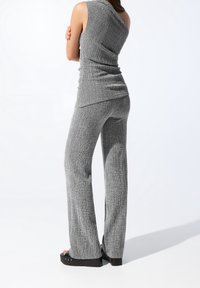 Szary, teksturowany sweter bez rękawów z drapowanym tyłem, połączony z dopasowanymi spodniami w szerokim kroju, które mają luźny krój.