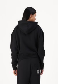 Μαύρη φαρδιά κουκούλα με κορδόνι, ριμπ μανσέτες και στρίφωμα. Διαθέτει μια μικρή διακοσμητική ετικέτα στην πίσω τσέπη. Μαλακό ύφασμα.