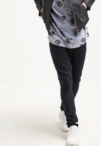 Black slim-fit pants made of soft fabric, paired with a grey floral-patterned shirt and white sneakers. Features a casual, relaxed design.