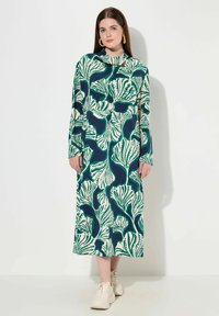 Långärmad klänning i mörkblått med stora gröna och krämfärgade bladmönster; lätt tyg; rund halsringning; design till ankeln.