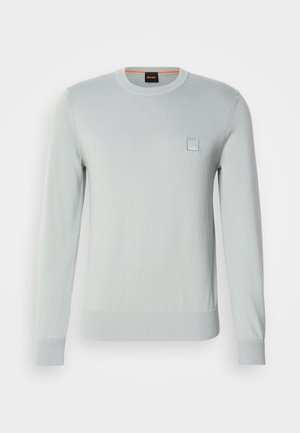 Svijetlosivi pleteni pulover s dugim rukavima, rebrastim rubovima i hemom, s malim plavim logom na prsima. Mekana, glatka tekstura.