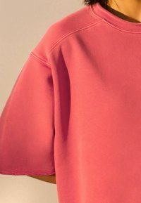 Roze oversized sweatshirt met korte mouwen, gemaakt van zacht materiaal. Heeft een ronde halslijn en een raw edge zoomafwerking.