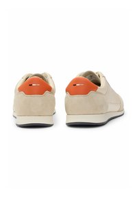 Sneakers in suede e pelle beige con un accento arancione sul tallone e dettagli neri e bianchi. Suola normale con motivo a spina di pesce.