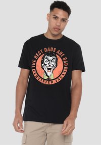 Black cotton t-shirt featuring a colorful graphic of a smiling clown with the text "THE BEST DADS ARE BAD CERTIFIED INSANE" in orange and white.