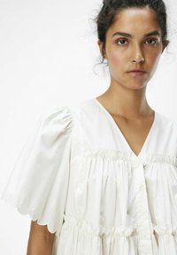 Weißes Baumwollkleid mit V-Ausschnitt, Knopfverschluss, puffartigen Ärmeln mit gewellten Kanten und gerafftem Design an der Brust und dem Rock.