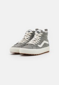 Zapatillas altas en gamuza gris con costuras blancas, cordones y una suela de goma. Presentan un parche con el logo en la lengüeta y una franja lateral.
