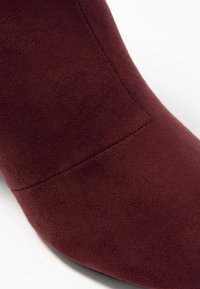 Burgundy mockaskstövlett med en slät yta, spetsig tå och subtil tonal sömnad längs sömmen.