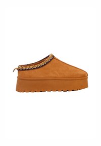 Brun ruskinds slip-on sko med en struktureret platformsål og et mønstret pynt ved kraven, med rundet tå og en trækflap bagpå.