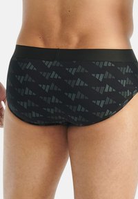 Musta alushousut, joissa on sileä vyötärö, tummanharmaalla geometrisella kuviolla, korostaen säihkettä, tiukkaa muotoilua.