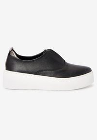 Black leather slip-on shoe with a textured finish, white platform sole, and a metallic accent on the back. Flat, round toe design.