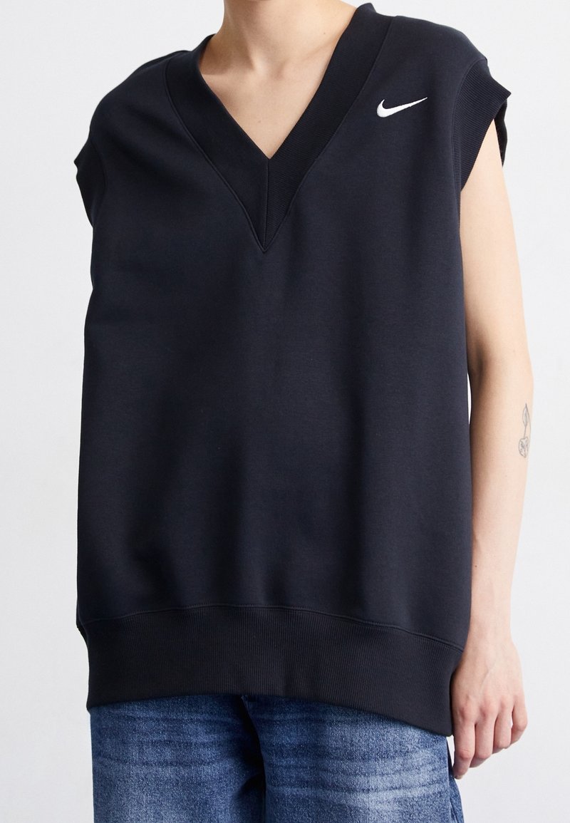 Svart ärmlös sweatshirt med djup V-hals, tillverkad av bomullsblandning, med en vit Nike-logotyp på vänster bröst och en ribbad fåll.