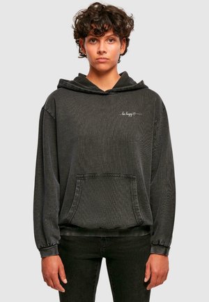 Czarny, oversize'owy hoodie z kieszenią z przodu i kapturem na sznurki. Napis „bądź szczęśliwy” w białej, kursywnej czcionce na górnej lewej części klatki piersiowej.