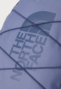 Purple fabric with a textured finish featuring an embossed logo. Elastic cord crosses over the surface, adding detail to the design.
