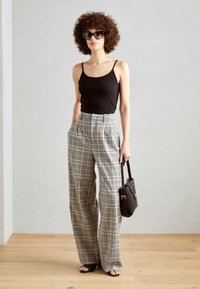 Karierte weite Hosen in Schwarz und Weiß mit rosa Akzenten, kombiniert mit einem schwarzen Tank-Top und schwarzen Sonnenbrillen. Kleine braune Handtasche.