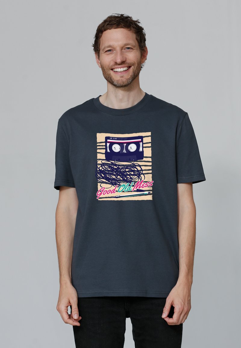 Donkergrijze katoenen t-shirt met een afbeelding van een cassetteband met kleurrijke tekst "Good Old Mess" en horizontale strepen als achtergrondaccenten.