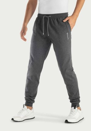 Grijze joggerbroeken met een elastische tailleband en trekkoord, met zijzakken en geribbelde manchetten. Gepaard met witte sportschoenen.