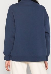 Mörkblå sweatshirt med hög krage, avslappnad passform och ribbad ärmslut. Mjuk textur, enkel design och rak fåll.