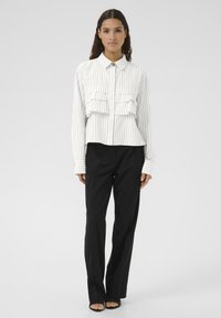 White and black striped shirt with a fitted design, featuring two chest pockets, full sleeves, and a collared neckline. Paired with black pants.