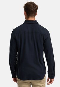 Camisa de manga larga azul marino hecha de tela texturizada con un corte holgado, con collar y puños abotonados, mostrando una vista trasera.