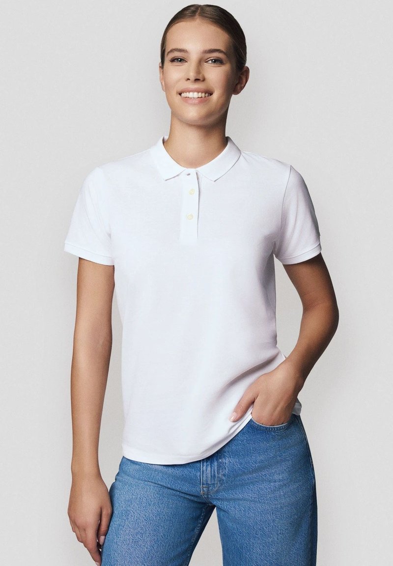 Biała koszulka polo z klasycznym kołnierzykiem, trzema żółtymi guzikami i krótkimi rękawami, połączona z jasnoniebieskimi dżinsami, gładka tekstura materiału.