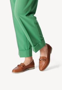 Ruske nahkakeermega loafers, millel on kummikreen ja millel on roheline üles keritud pükste paar. Kingadel on sile pind ja ümar varvas.