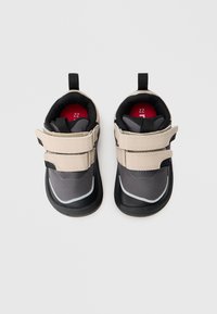 Sapatos infantis pretos e cinzentos com tiras bege, material texturizado, forma arredondada e peças para puxar. Etiqueta de tamanho "22" em vermelho visível por dentro.