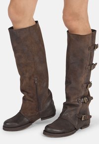 Hnědé semišové kozačky po kolena se zipovým uzavřením, vybavené několika přezkami a kulatou špičkou. Texturovaný povrch a plochý podpatek.