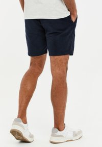 Pantalones cortos de pana color navy con bolsillos laterales, terminados por encima de la rodilla. Combinados con zapatillas deportivas blancas y grises.