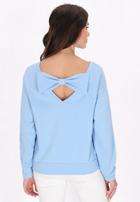 Felpa azzurra chiara con maniche lunghe e scollo ampio. Retro con apertura a chiave e dettaglio di grande fiocco. Tessuto morbido e vestibilità rilassata.