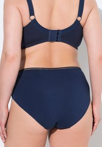 Reggiseno blu navy con spalline larghe, ganci regolabili e un slip a vita alta abbinato. Texture liscia con un colore uniforme, senza motivi visibili.