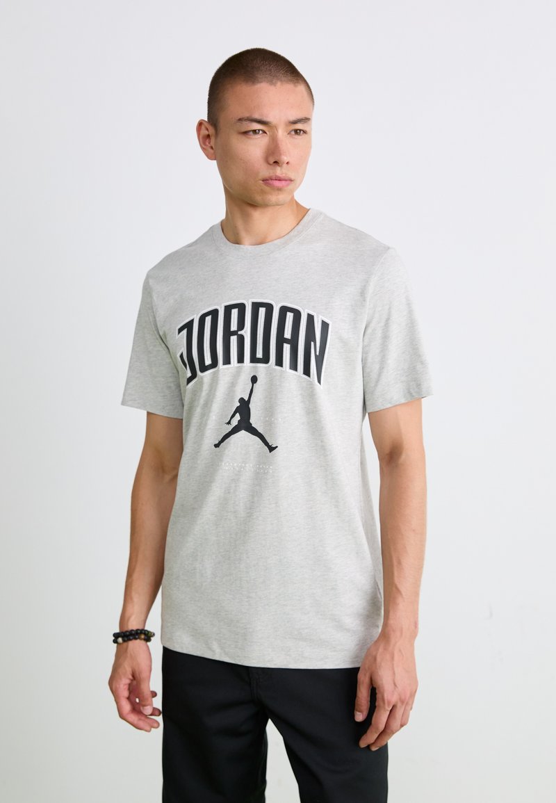 Grå bomulds t-shirt med et sort "JORDAN" logo og Jumpman grafik trykt på forsiden. Korte ærmer og rund halsudskæring.