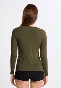 Maglia a maniche lunghe di colore verde oliva con una texture liscia, con scollo rotondo e design aderente, abbinata a pantaloni corti neri.
