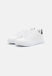 Hvide sneakers med en glat læderoverdel, rund tå, snørebånd og en kontrastfarvet sort hælaccent, samt en struktureret gummisål.